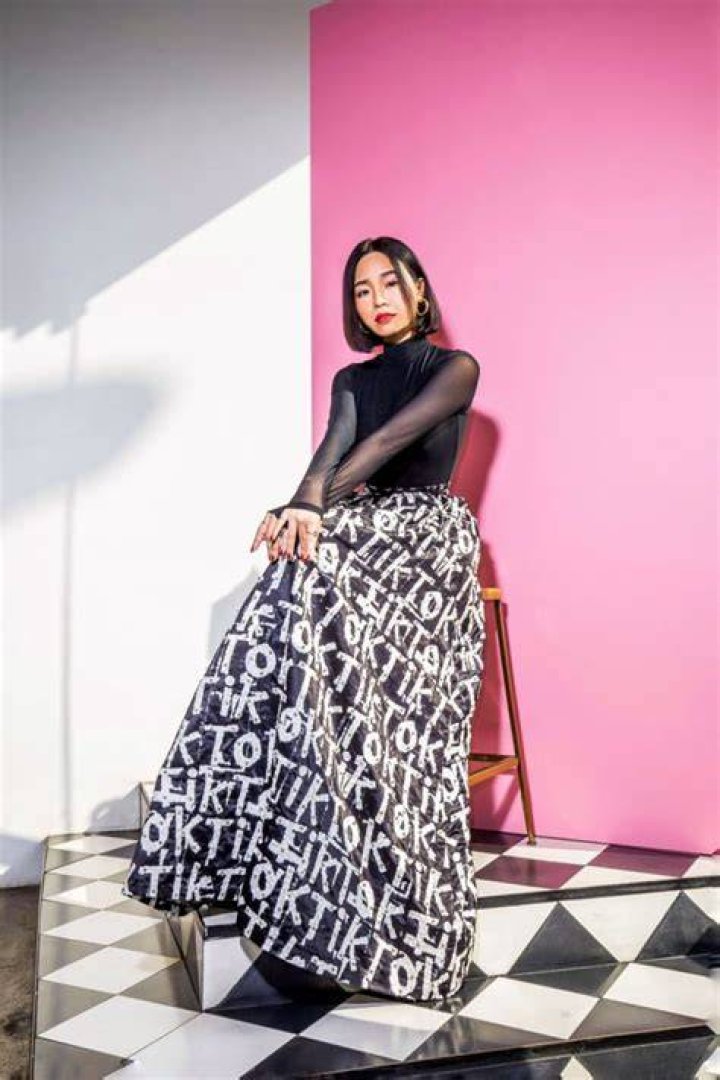 cece vu stands on a balcony with palm trees in the background wearing a full length hot pink dress