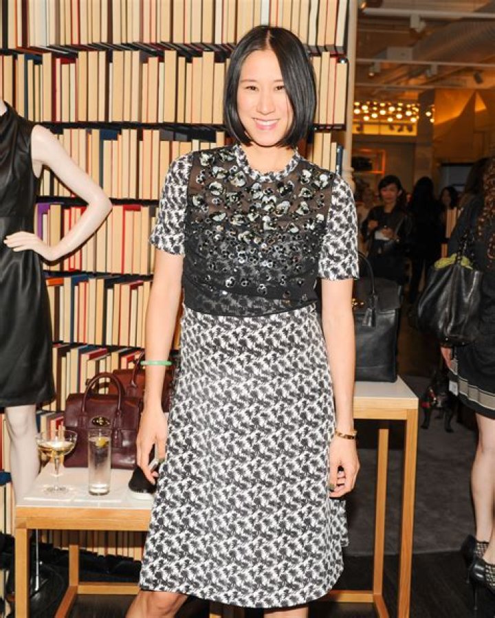 eva chen stands in front of a marble statue in the city wearing a plaid one shoulder dress with an asymmetrical hem in black and yellow along with snakeskin boots