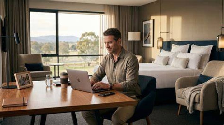 man working away from home on business trip, sitting on sofa and checking phone with feet up