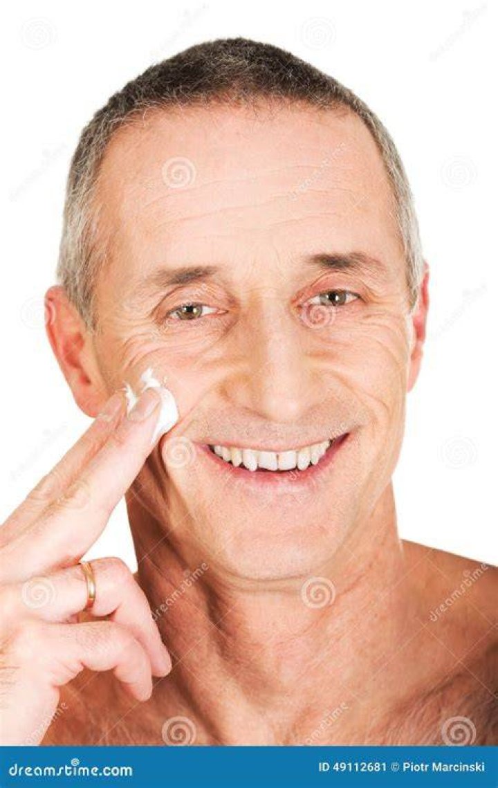 mature man applying face cream while looking in mirror at bathroom