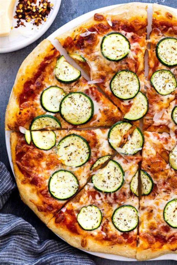 vegetarian pizza with zucchini, sun dried tomatoes source pesto, spinach, seeds and nuts flat lay top down composition on wooden background