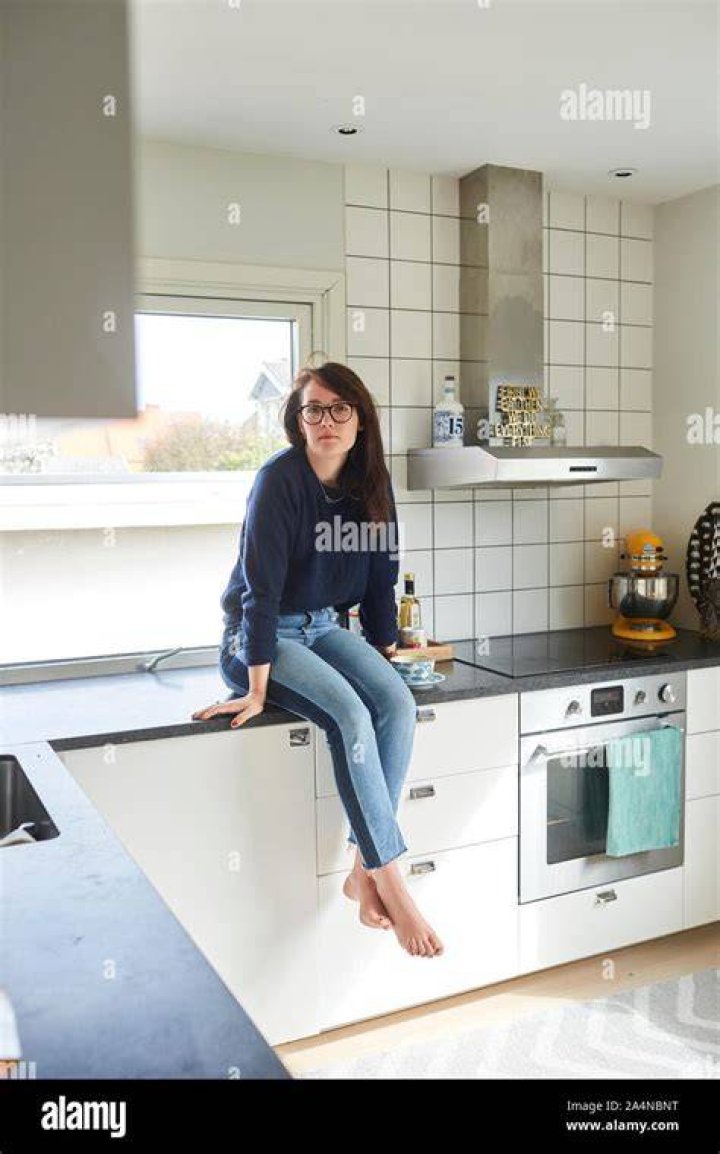 Young couple kissing at the kitchen counter young woman sitting on kitchen counter, kissing and embracing her boyfiend standing in front of her